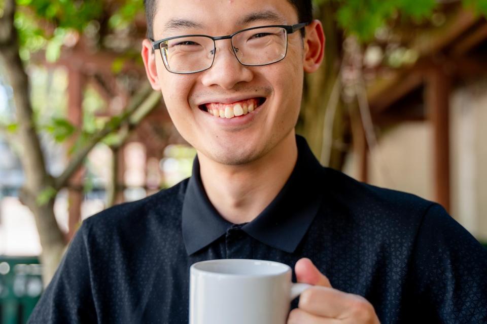 A picture of a man holding a mug underneath green foliage,